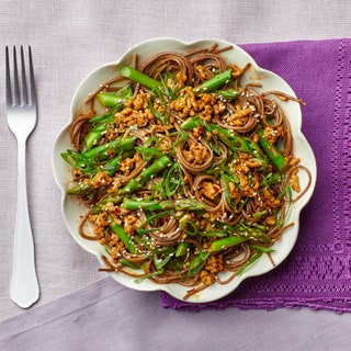 Bowl of pork and asparagus soba garnished with sesame seeds and scallions sitting next to a purple napkin