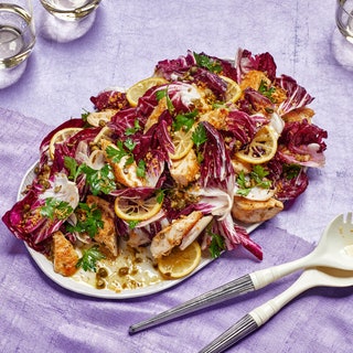 Platter of warm chicken piccata salad with radicchio parsley and capers topped with sliced lemons