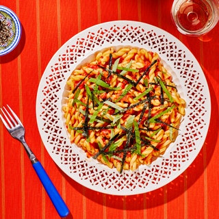 Decorative bowl of tomato pasta on a red striped tablecloth.