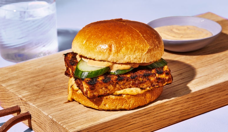 A big slab of grilled tofu on a hamburger bun, topped with "special sauce" and sliced cucumbers.