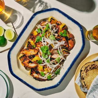 A platter of al pastor chicken garnished with cilantro and onions next to a plate of tortillas.