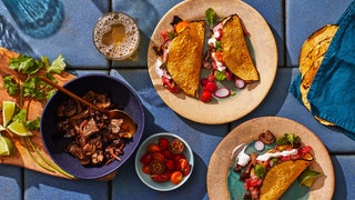 A spread of spiced mushroom tacos with toppings including lime wedges cilantro charred tortillas and more.