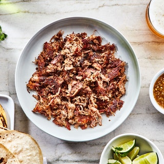 A bowl of shredded carnitas surrounded by taco toppings.