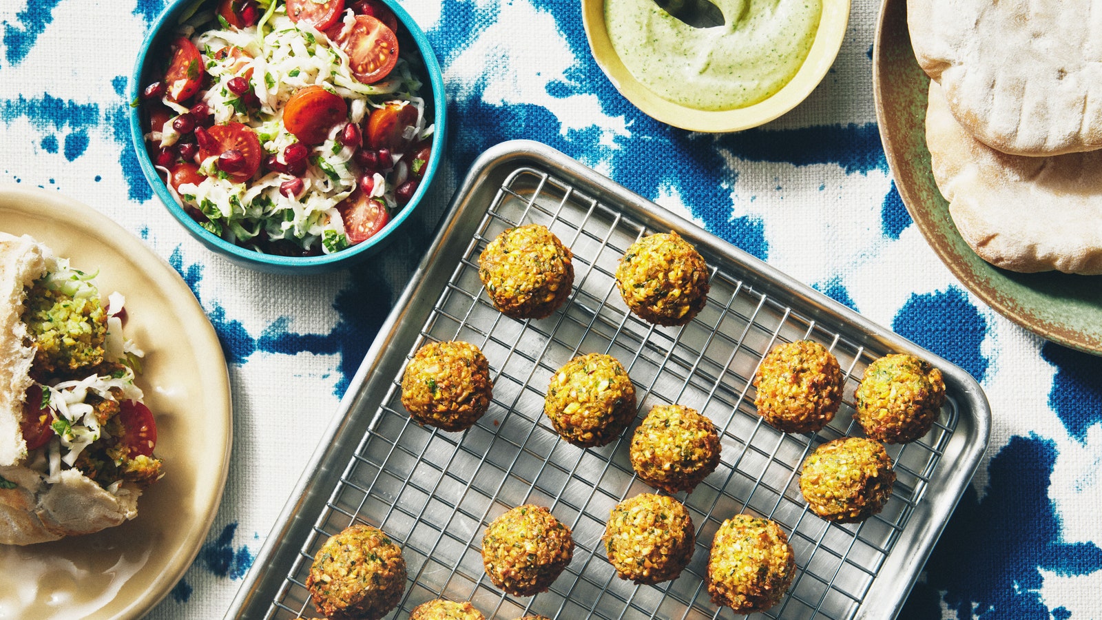 Falafel on a wire rack with pita spiced green tahini sauce and shredded cabbage salad with pomegranate seeds and tomatoes.