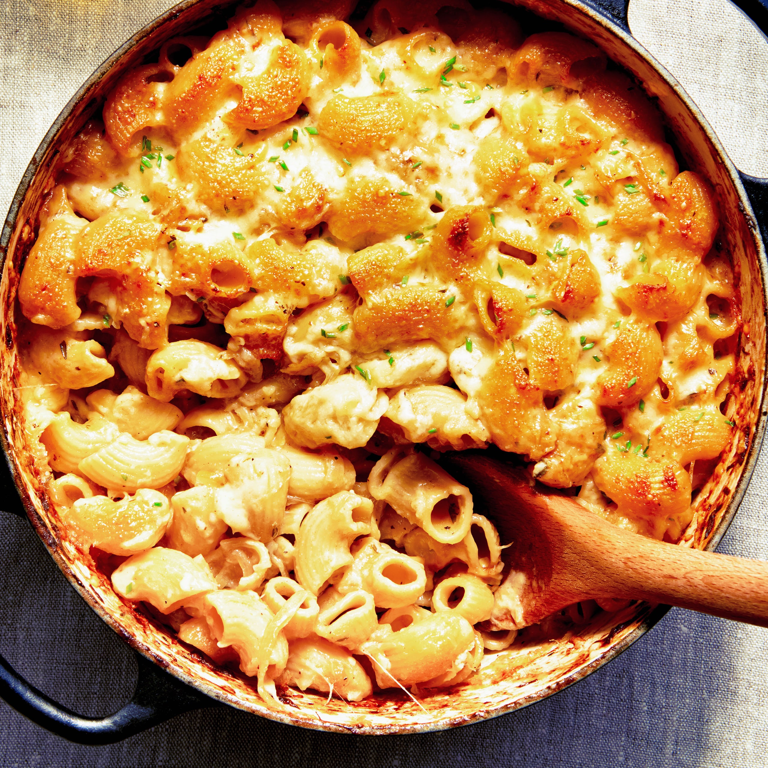 Pasta with cheese and caramelized onions in a dutch oven with a wooden spoon.