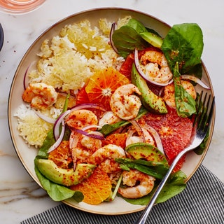 A dish of crispy rice topped with shrimp sliced avocado orange and grapefruit rounds and greens.